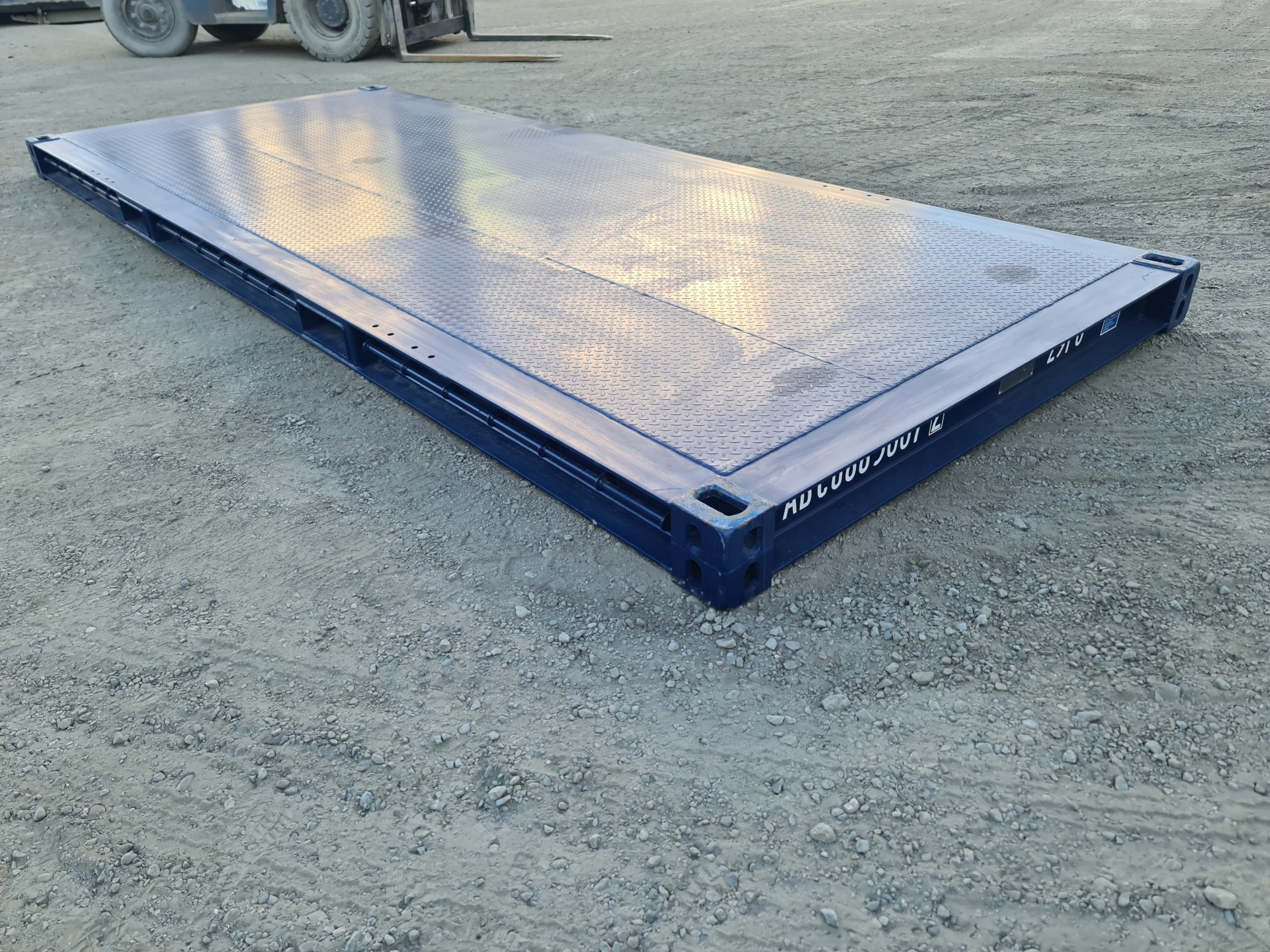 A deep blue 20ft long bolster/platform container on the ground. Sunlight is reflecting off of its glossy paint.