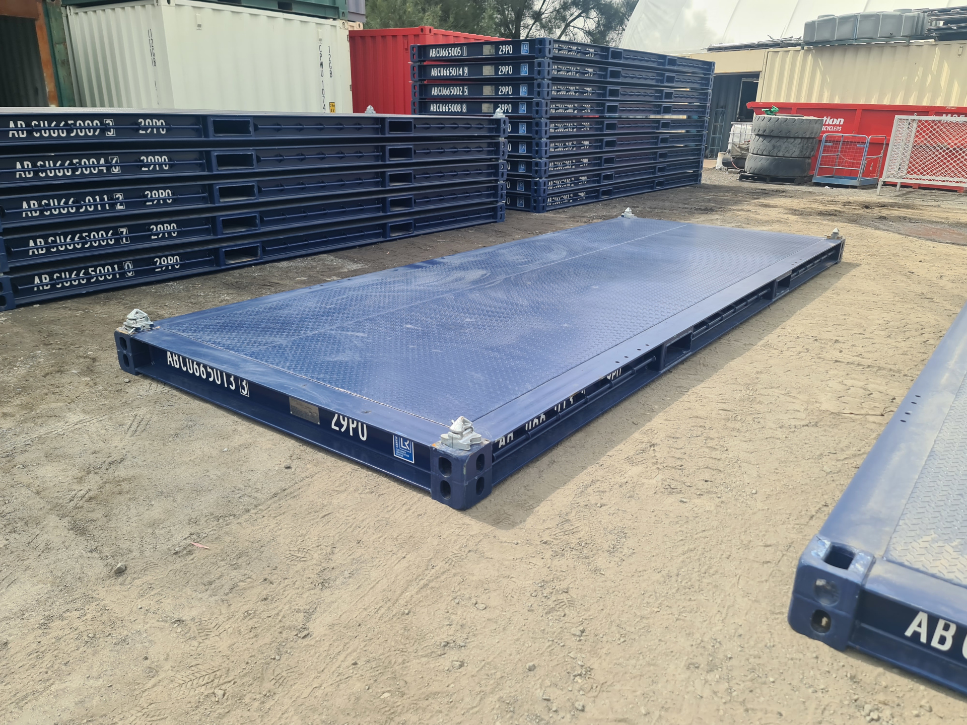 A deep blue 20ft platform container laying on the ground. A stack of identical containers can be seen in the background.