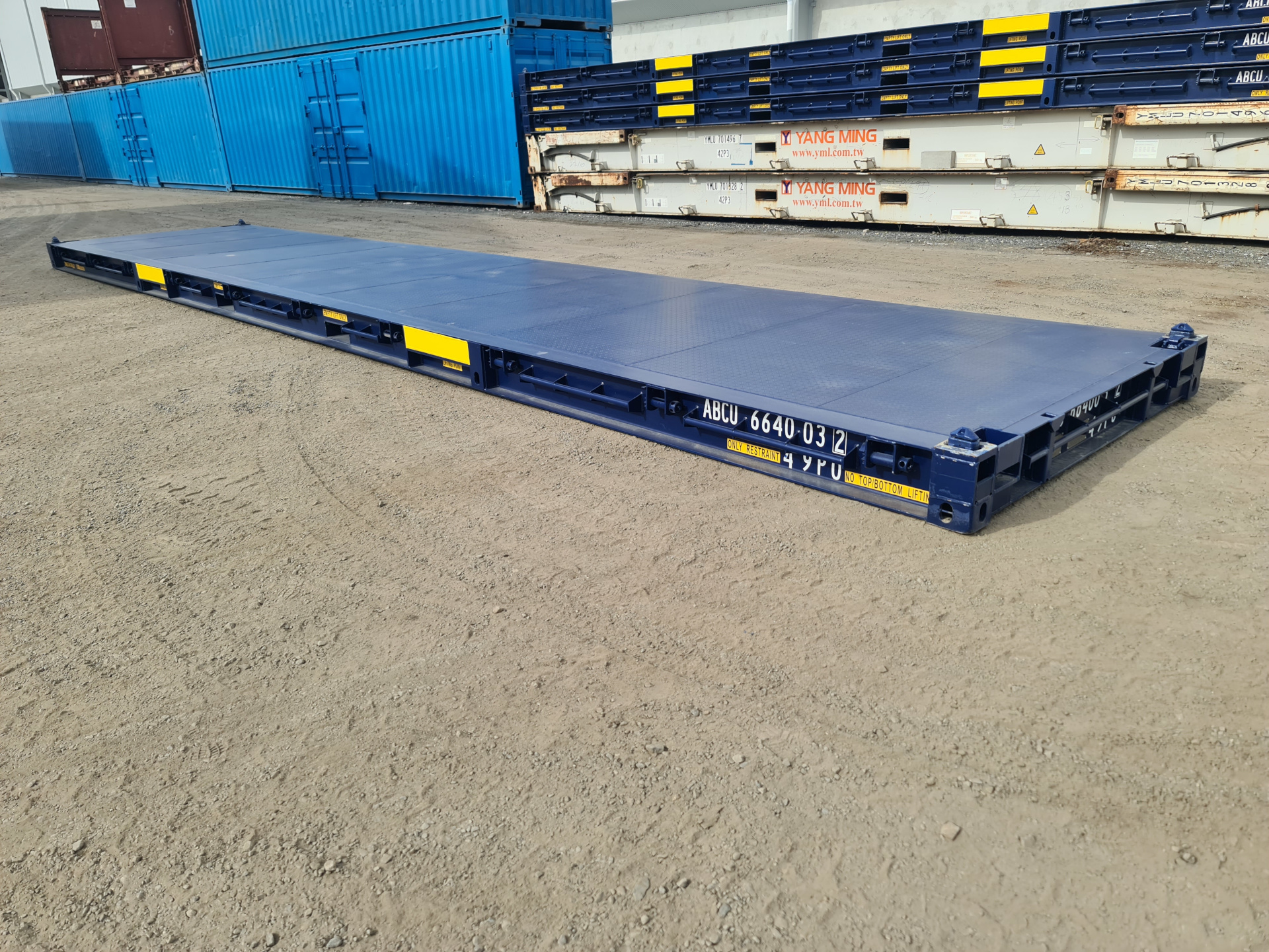 A deep blue 40ft platform container laying on the ground. A stack of multiple different types of containers can be seen in the background.